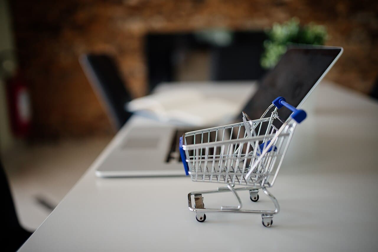 A miniature shopping cart beside a laptop on a desk